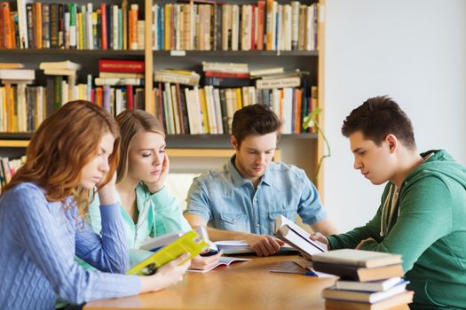 people, knowledge, education and school concept - group of students reading books and preparing to exam in library