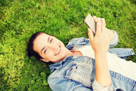 lifestyle, summer vacation, technology and people concept - smiling young girl with smartphone lying on grass in park