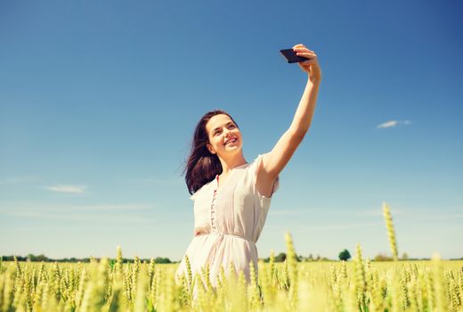 happiness, nature, summer, vacation and people concept - smiling young woman with smartphone on cereal field