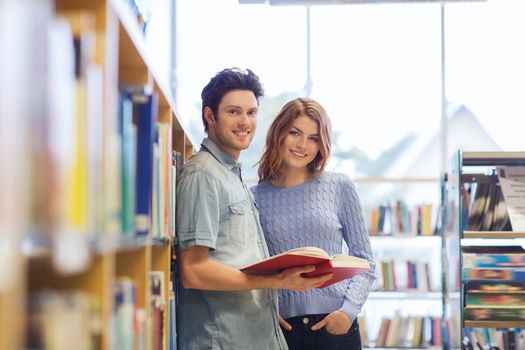 people, knowledge, education and school concept - happy student couple with books in library