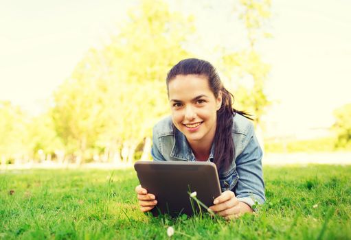 lifestyle, summer vacation, technology, leisure and people concept - smiling young girl with tablet pc computer lying on grass in park