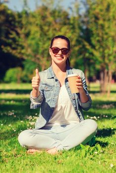 lifestyle, summer vacation, drinks and people concept - smiling young girl drinking coffee from paper cup and showing thumbs up in park