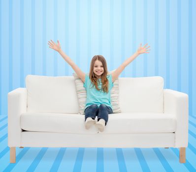 home, leisure, people and happiness concept - smiling little girl sitting on sofa with raised hands over blue striped background