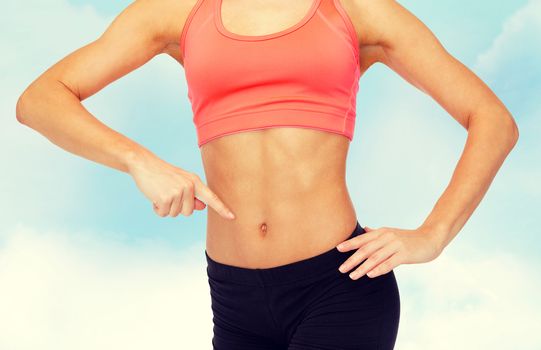 fitness, exercise and diet concept - close up of woman pointing finger at her six pack