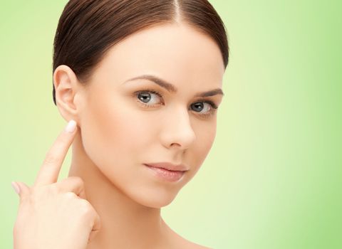 people, beauty, hearing and healthcare concept - face of beautiful woman touching her ear over green background