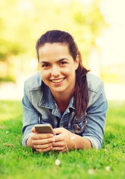 lifestyle, summer vacation, technology, leisure and people concept - smiling young girl with smartphone lying on grass in park