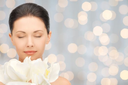 beauty, people, holidays and health concept - beautiful young woman smelling flowers with closed eyes over lights background