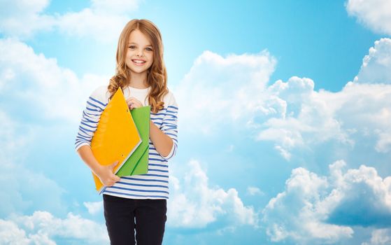 education, people, children and school concept - happy girl holding colorful folders over blue sky with clouds background