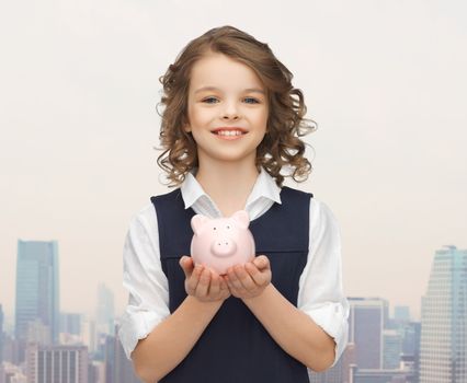 people, money, finances and savings concept - happy girl holding piggy bank on palms over city background