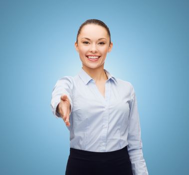 business, gesture and education concept - friendly young smiling businesswoman with opened hand ready for handshake over blue background