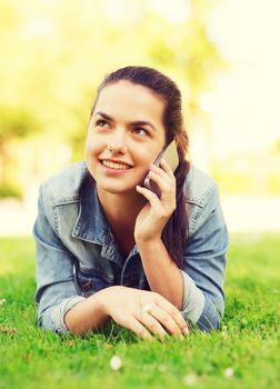 lifestyle, summer vacation, technology, leisure and people concept - smiling young girl with smartphone talking and lying on grass in park