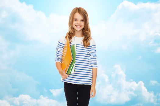 education, people, children and school concept - happy girl holding colorful folders over blue sky with clouds background