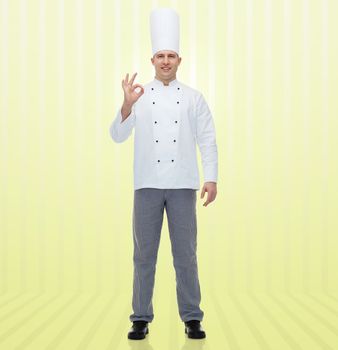 cooking, profession, gesture and people concept - happy male chef cook showing ok sign over yellow background