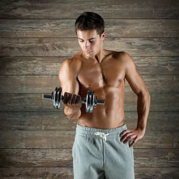 sport, fitness, weightlifting, bodybuilding and people concept - young man with dumbbell flexing biceps over wooden wall background