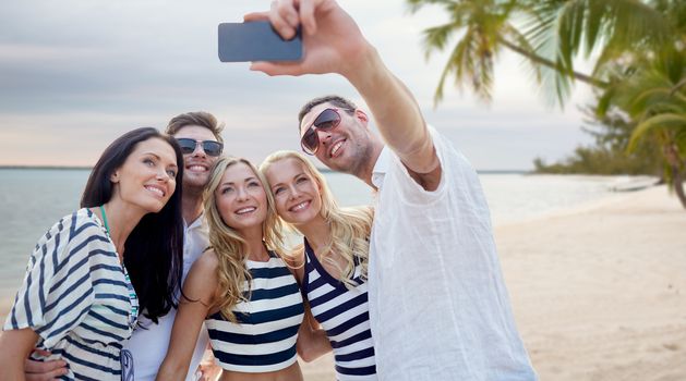summer, sea, tourism, technology and people concept - group of smiling friends with smartphone photographing and taking selfie on beach