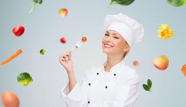 cooking and food concept - smiling female chef, cook or baker with fork and tomato over falling vegetables on gray background