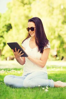 lifestyle, summer, vacation, technology and people concept - smiling young girl with tablet pc sitting on grass in park