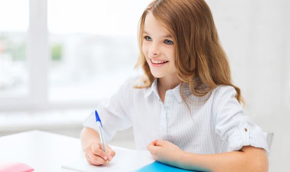 education and school concept - little student girl writing in notebook at school