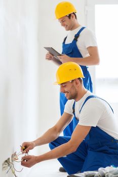 building, renovation, technology, electricity and people concept - two builders with tablet pc computer fixing wiring indoors