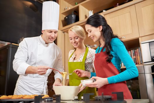 cooking class, culinary, bakery, food and people concept - happy group of women and male chef cook baking muffins in kitchen