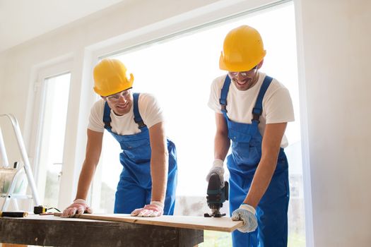 business, building, teamwork and people concept - group of smiling builders in hardhats with tools indoors