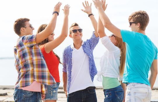 friendship, leisure, summer, gesture and people concept - group of smiling friends making high five outdoors