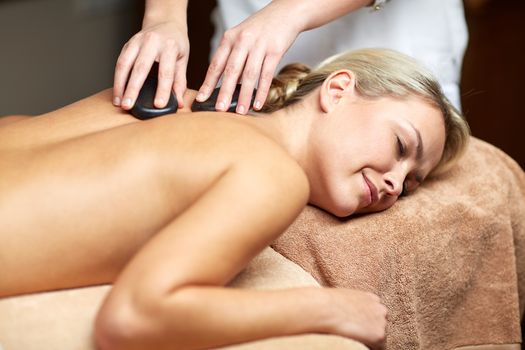 people, beauty, spa, healthy lifestyle and relaxation concept - close up of beautiful young woman having hot stone massage in spa