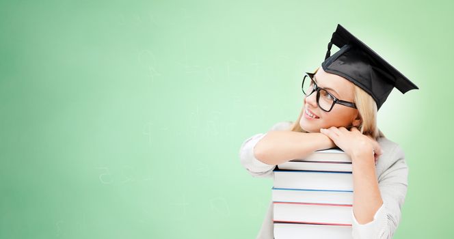 education, happiness, graduation and people concept - picture of happy student in mortar board cap with stack of books daydreaming over green background
