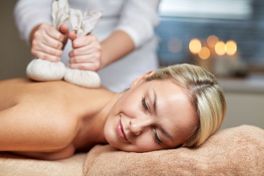 people, beauty, spa, healthy lifestyle and relaxation concept - close up of beautiful young woman lying and having herbal bag massage in spa