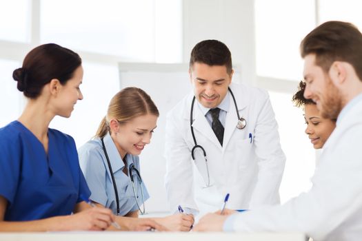 hospital, profession, people and medicine concept - group of happy doctors meeting and taking notes at medical office