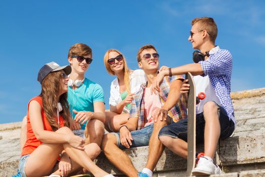 friendship, leisure, summer and people concept - group of smiling friends with skateboard sitting on city street