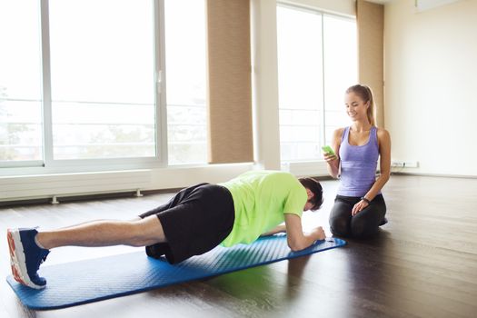 fitness, sport, technology and people concept - man and woman with smartphone doing plank exercise on mat in gym