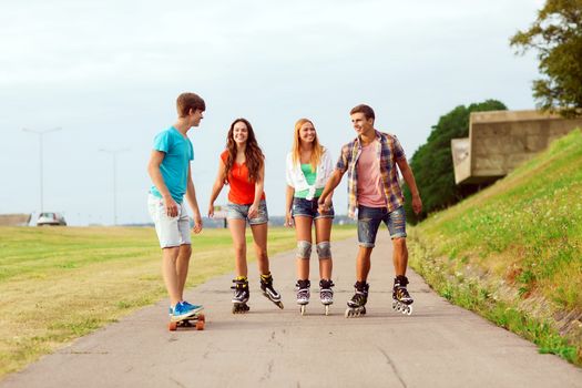 holidays, vacation, love and friendship concept - group of smiling teenagers with roller skates and skateboard riding outdoors