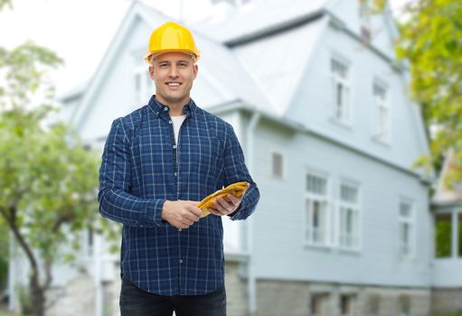 repair, building, construction and maintenance concept - smiling man in helmet with gloves over living house background