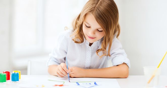 education, school, art and painitng concept - little student girl painting at school