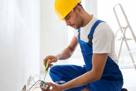 building, renovation, technology, electricity and people concept - builder with screwdriver fixing socket indoors