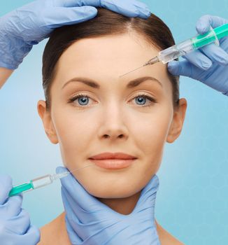 plastic surgery, injections and beauty concept - beautiful young woman face and surgeon hands with syringes over blue background