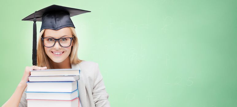 education, happiness, graduation and people concept - picture of happy student in mortar board cap with stack of books over green background