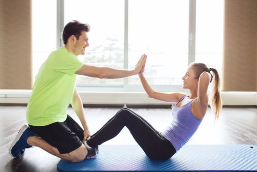 fitness, sport, training, teamwork and people concept - happy woman with personal trainer doing sit ups and high five gesture in gym