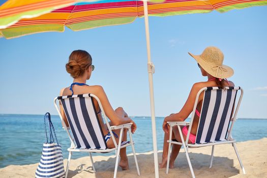 summer vacation, travel and people concept - happy women sunbathing in lounges on beach