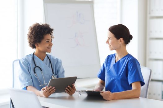 hospital, profession, people and medicine concept - group of happy doctors with tablet pc computer and clipboard meeting at medical office