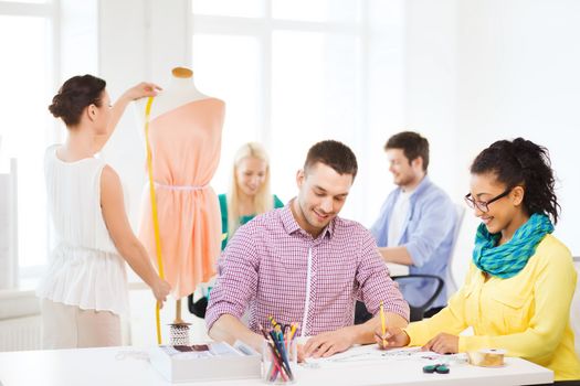 startup, education, fashion and office concept - smiling designers drawing sketches and adjusting dress on mannequin in office