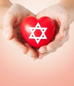 religion, christianity, jewish community and charity concept - close up of female hands holding red heart with star of david symbol over beige background