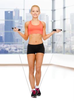 sport, fitness, people and weight loss - smiling sporty woman jumping with skipping rope over gym background