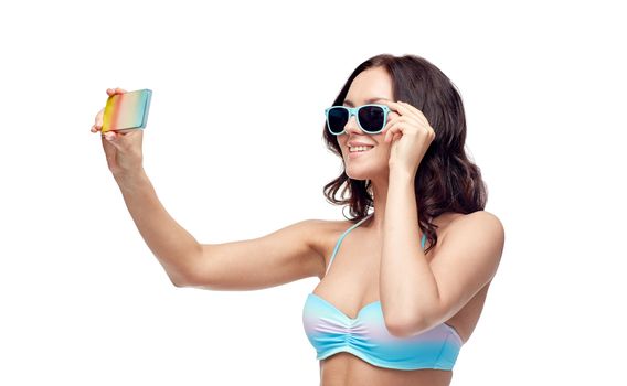 people, technology, summer and beach concept - happy young woman in bikini swimsuit and sunglasses taking selfie with smatphone