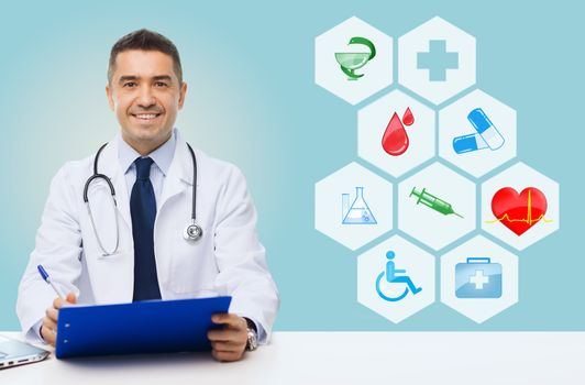 medicine, profession, technology and people concept - happy male doctor with clipboard and stethoscope over blue background with medical icons