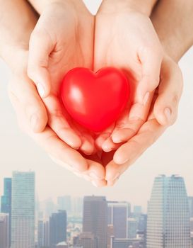 health, love and relationships concept - close up of couple hands with big red heart over city skyscrapers background