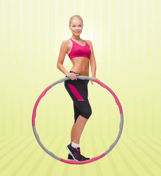 fitness, sport, people and healthcare concept - young sporty woman exercising with hula hoop over yellow striped background