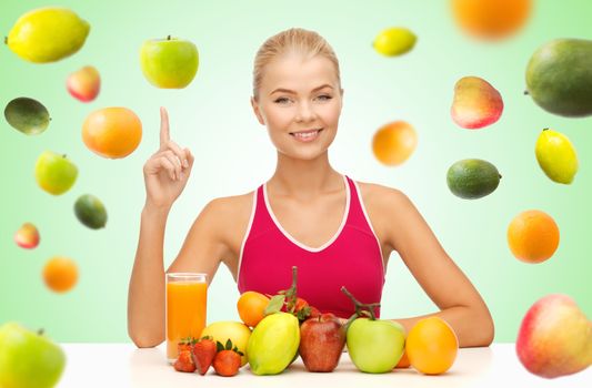 healthy eating, diet, detox and people concept - happy young woman with organic food or fruits pointing finger up over green background with falling fruits