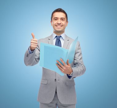 business, people, finances and paper work concept - happy smiling businessman in suit holding folder and showing thumbs up over blue background